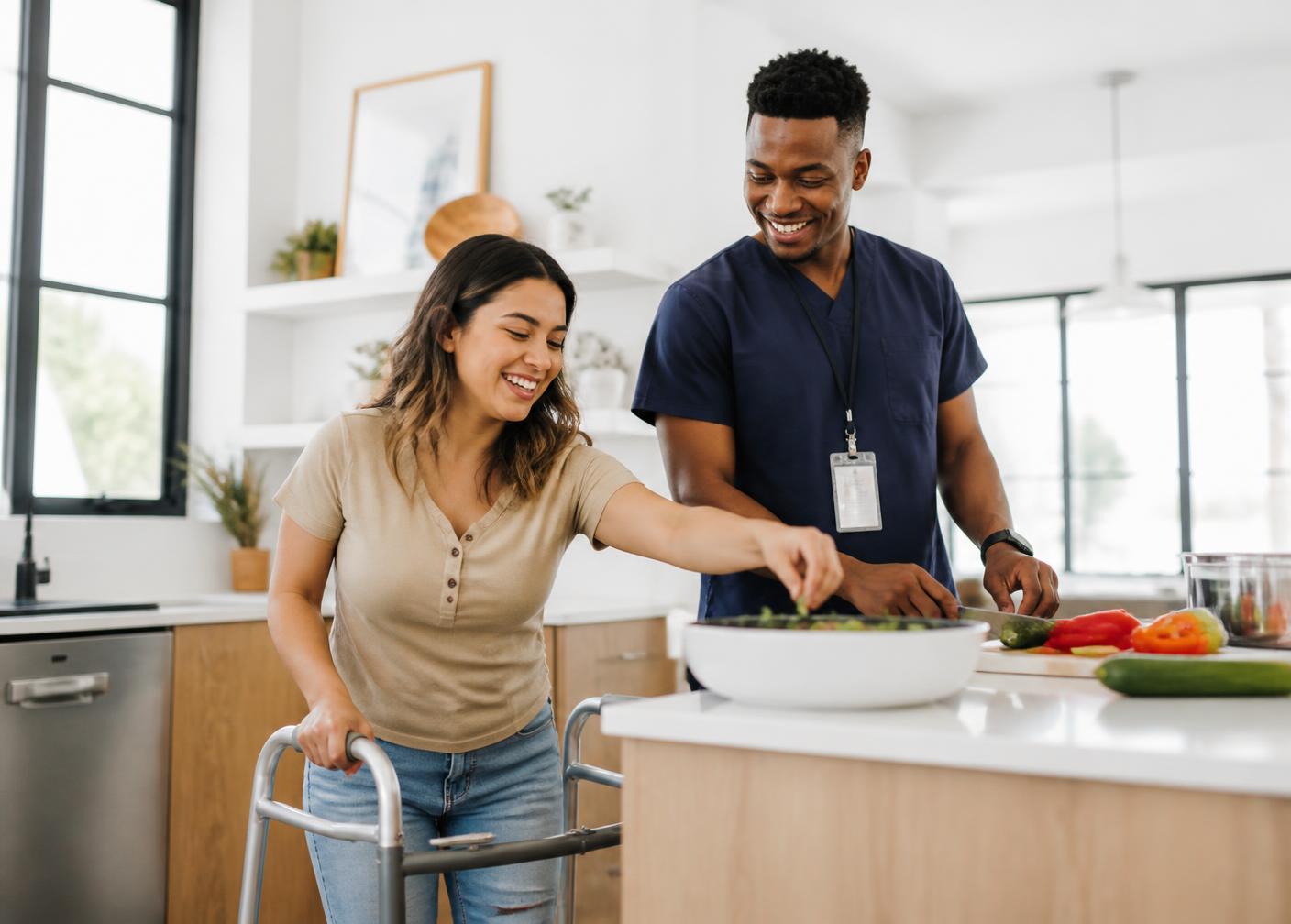 A young woman using a walker cooking with her support attendant in a bright kitchen